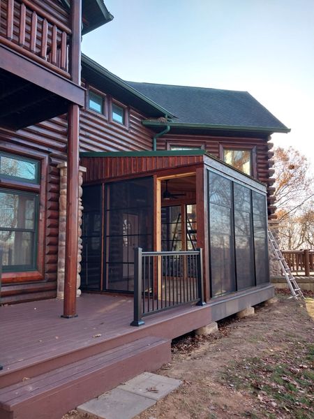 Four-season room addition built onto a log home, with board siding and black railings